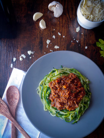 zucchini noodles on a blue plate with parmesan in a bowl and garlic in background