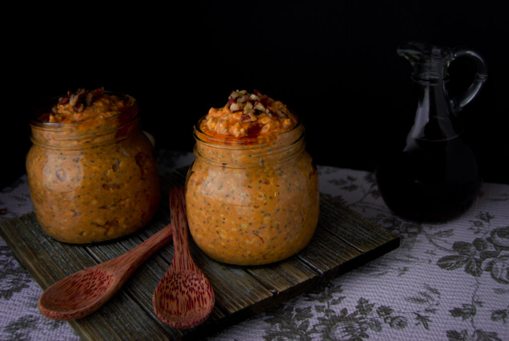 Two Mason jars full of pumpkin pie overnight oats topped with pecans and maple syrup