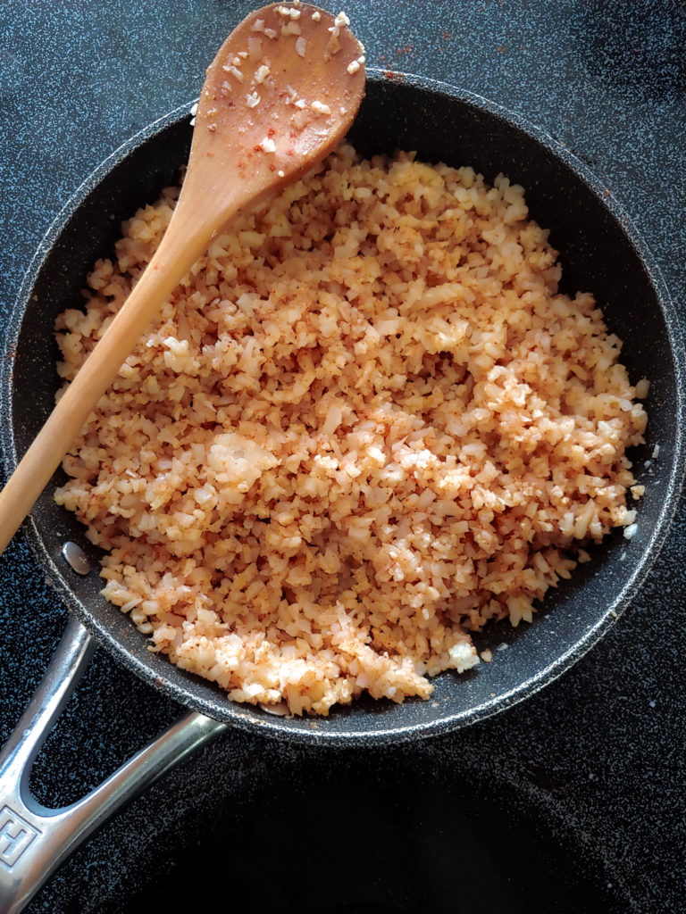 cauliflower rice in a pan with wooden spoon