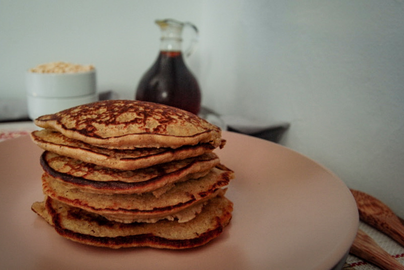 stack of apple oat cinnamon pancakes with maple syrup in the background