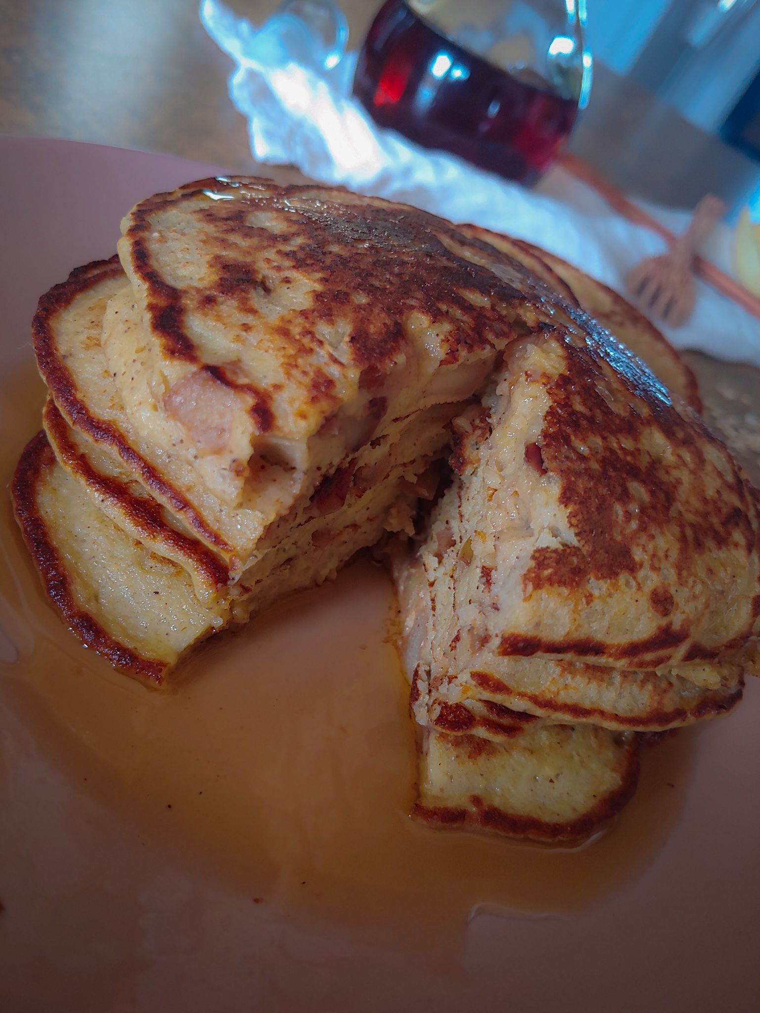 stack of apple cinnamon oat pancakes with a slice cut out maple syrup in background